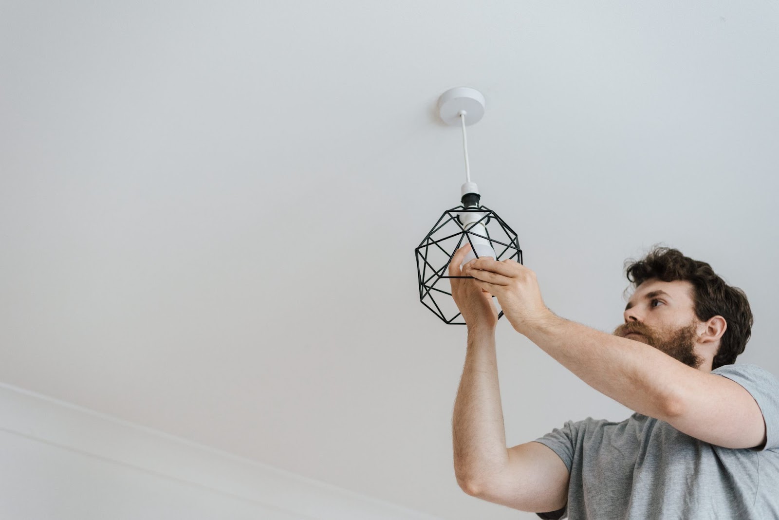 A shot from below of a bearded man screwing in a lightbulb